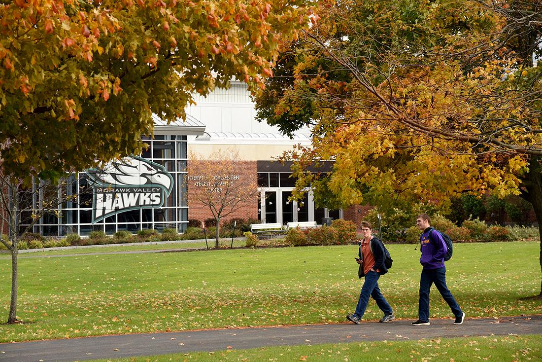 Two students walk under fall foliage during autumn at the Utica Campus