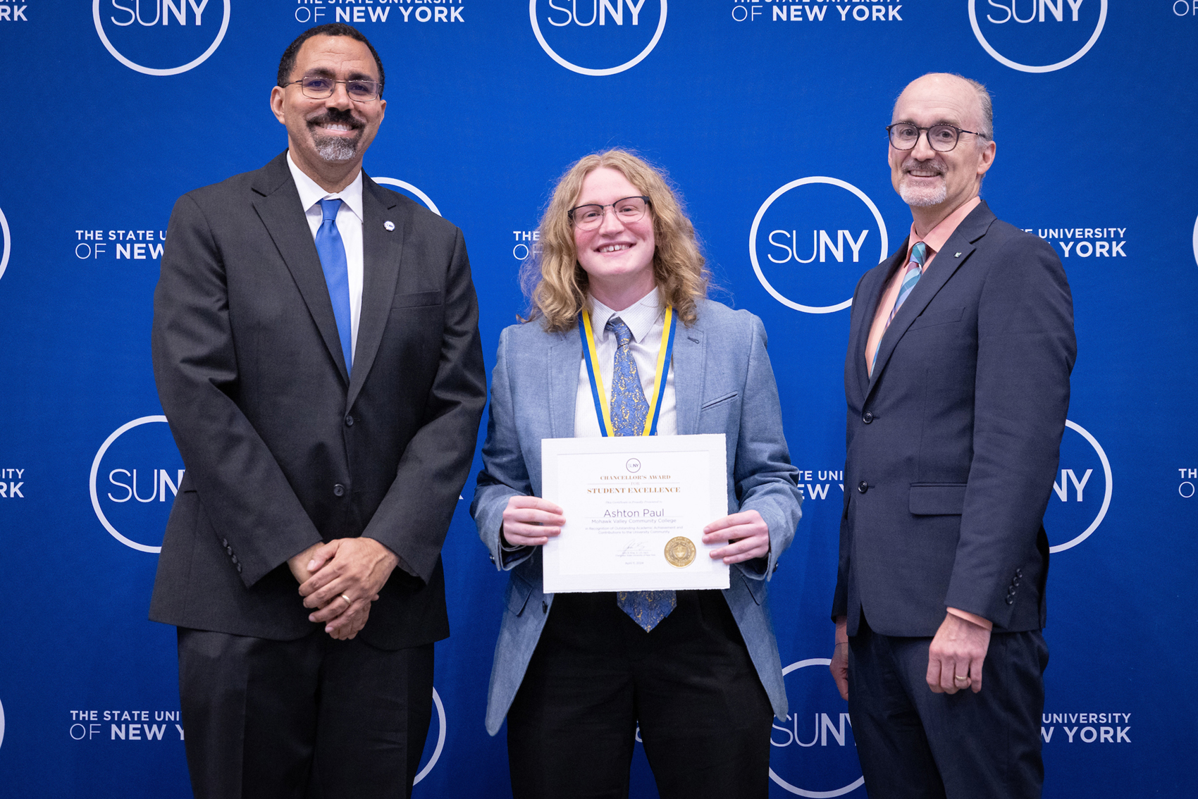 Three people standing in front of blue SUNY backdrop