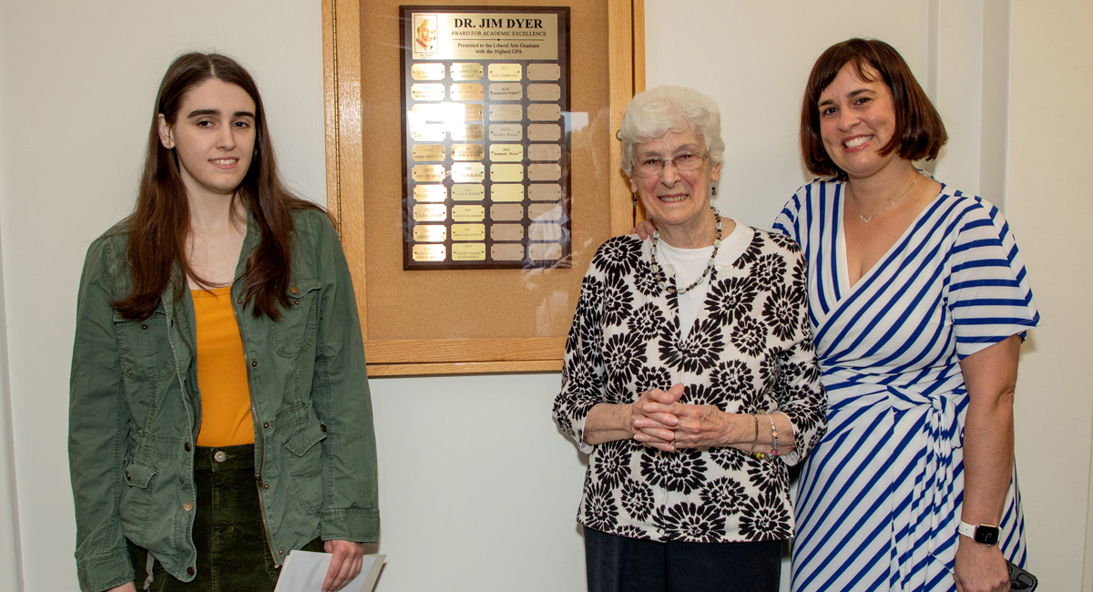 Three people standing in front of Jim Dyer Award plaque: Amanda Moyer, Madeline Dyer, Jennifer Campbell