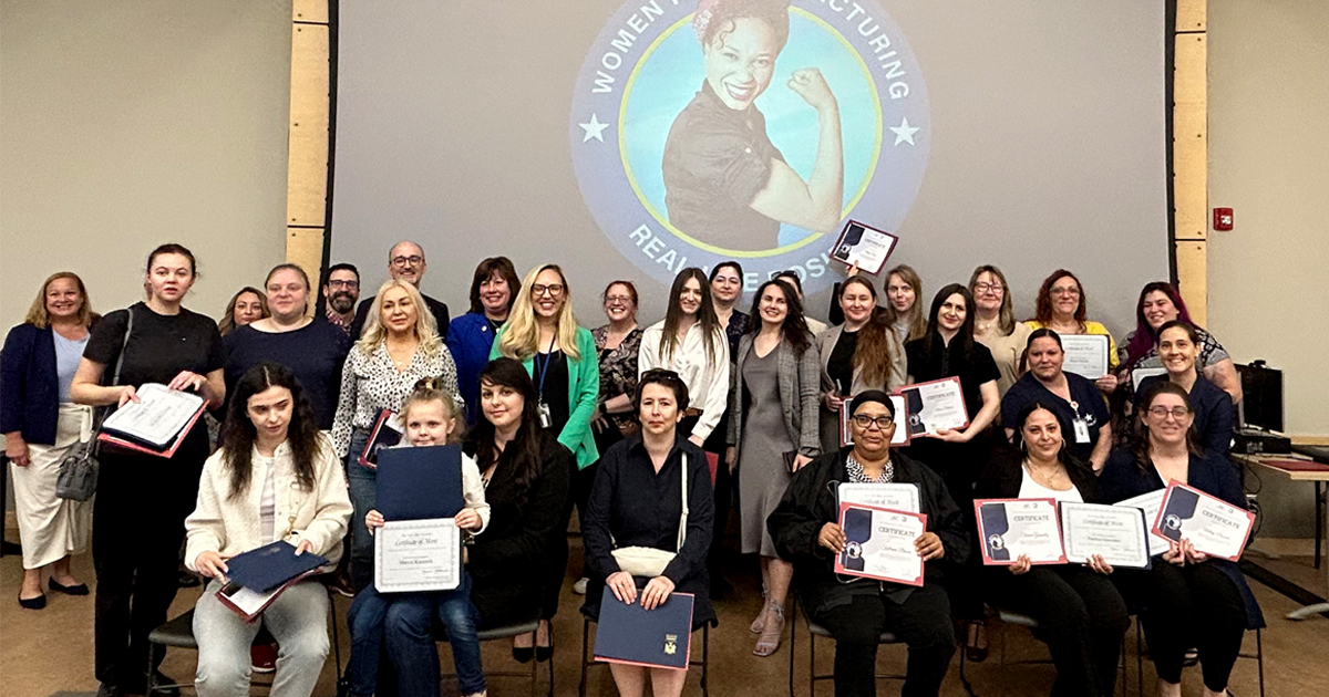 Group of people smiling, holding certificates, in front of Real Life Rosies screen