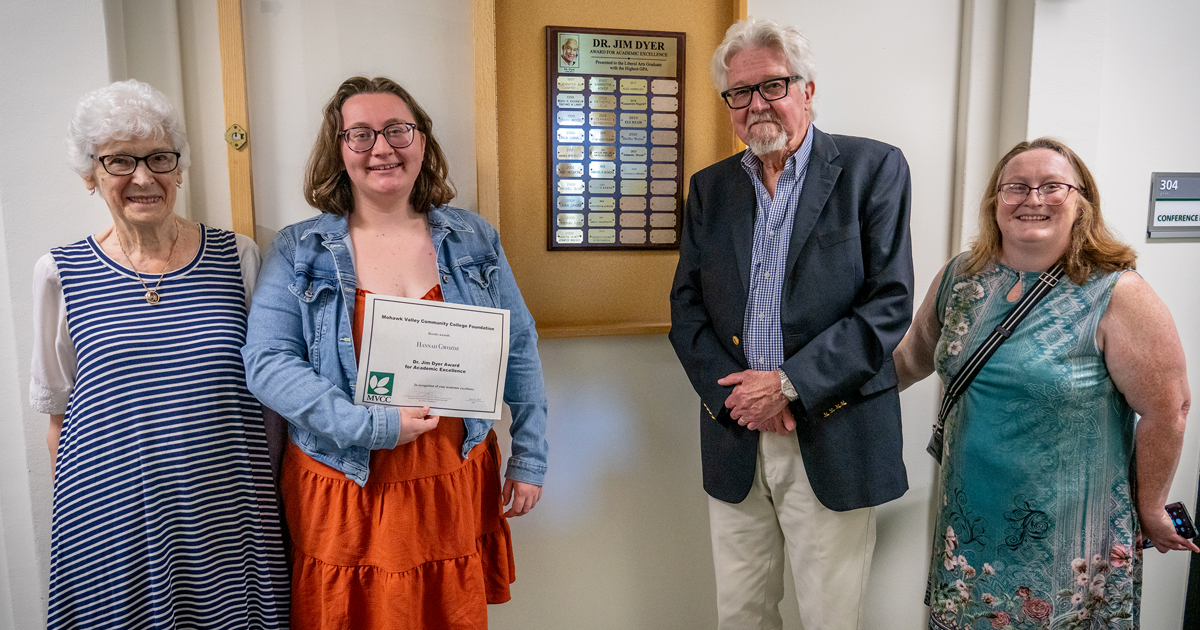2025 Dr. Jim Dyer Award winner Four people standing next to award plaque on wall