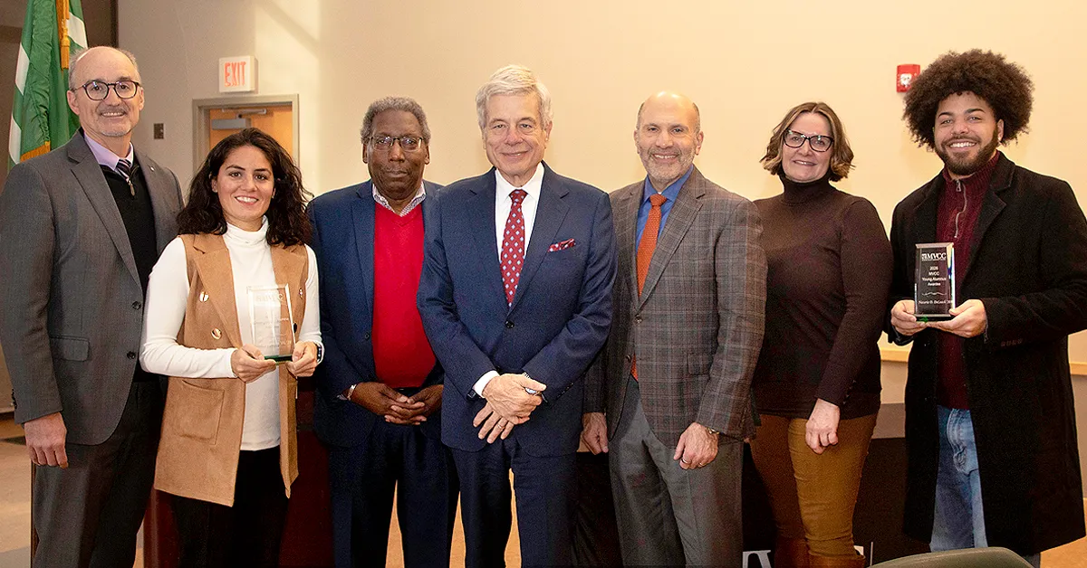 Seven people stand side by side indoors, smiling; two hold glass awards