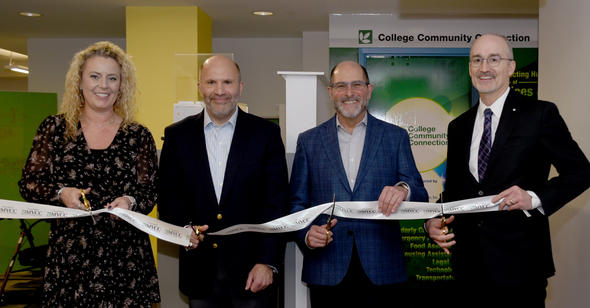 Four people standing, smiling, holding scissors to cut ribbon